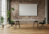 Modern industrial meeting room with a large conference table, two black office chairs, a projector screen on an exposed brick wall, and abundant natural light from large windows. Features hardwood floors and various green plants, suitable for collaborative workspaces